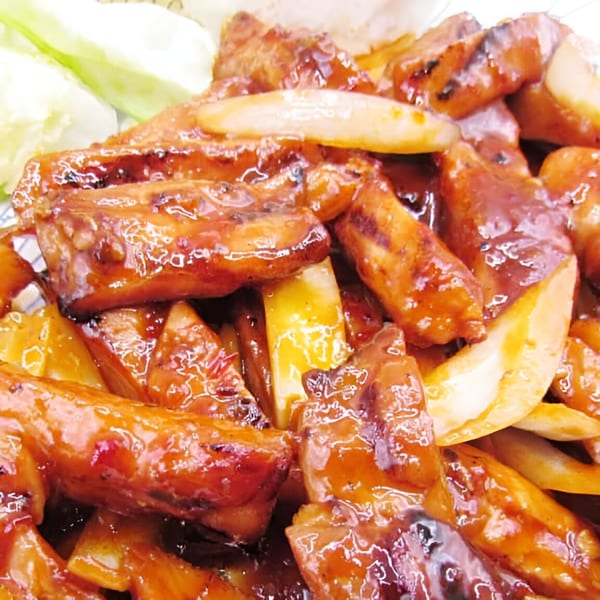 Close-up of Lucky Teriyaki's glazed chicken and onions, with a side of fresh cucumber.