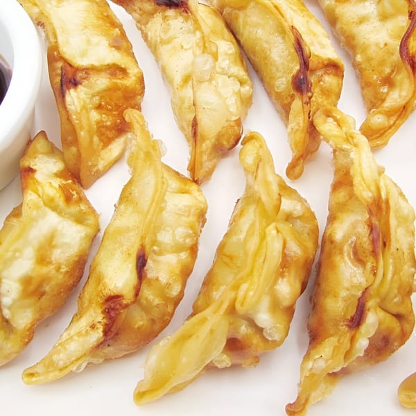 Close-up of golden-brown fried gyoza dumplings with a small bowl of dipping sauce.